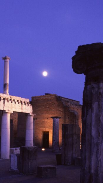 The moon shines over Pompeii ruins illuminated by warm light at night, HD Mobile Wallpaper