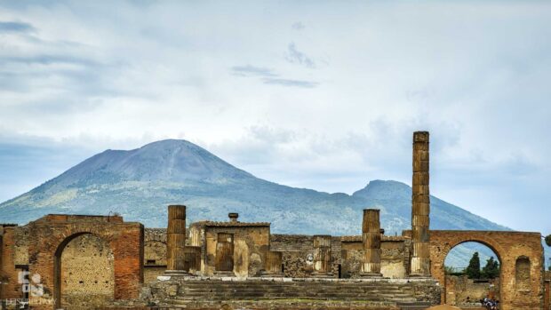 The ruins of Pompeii stand with Mount Vesuvius in the background under a cloudy sky, HD Desktop Wallpaper