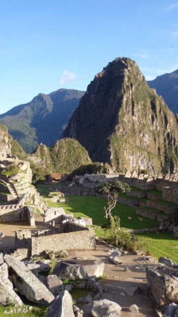 The Peru Wallpapers display an ancient stone ruin site surrounded by green mountains under a clear blue sky, HD Phone Wallpaper
