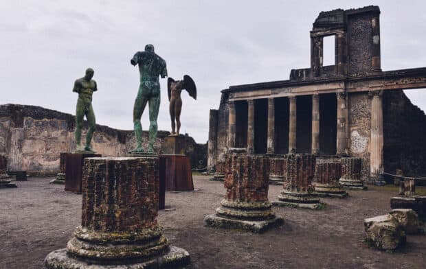 The ruins of Pompeii feature ancient statues and columns under a cloudy sky, 2K Desktop Wallpaper