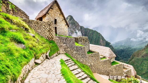 Ancient stone buildings stand on a lush hill with mountains in the background in Peru, HD Desktop Wallpaper