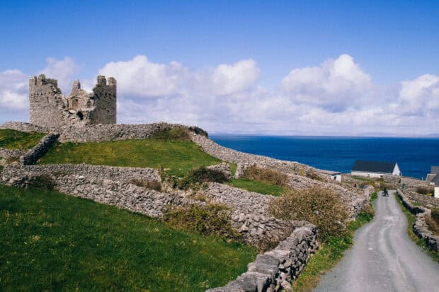 A cyclist rides along a winding road near an ancient stone castle on The Aran Islands with the ocean in the background, HD Desktop Wallpaper