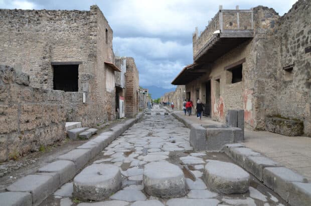 A historic stone paved street in Pompeii shows ancient ruins under a cloudy sky, HD Desktop Wallpaper