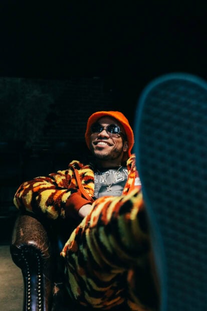 Anderson Paak is sitting relaxed in a bright orange and yellow outfit with sunglasses, HD Mobile Wallpaper
