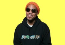 Anderson Paak wearing sunglasses and an orange beanie smiling in front of a yellow background, HD Desktop Wallpaper