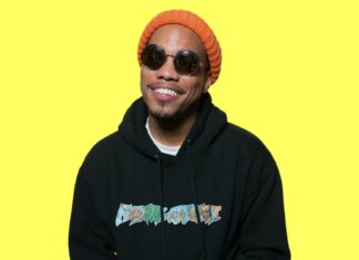 Anderson Paak wearing sunglasses and an orange beanie smiling in front of a yellow background, HD Desktop Wallpaper