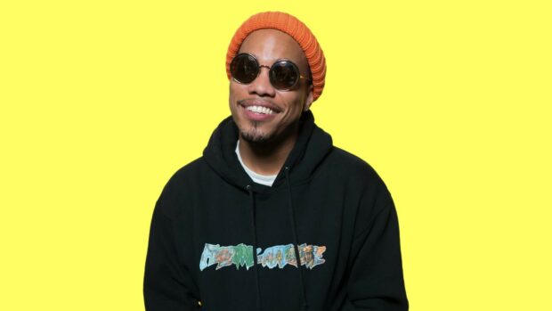 Anderson Paak wearing sunglasses and an orange beanie smiling in front of a yellow background, HD Desktop Wallpaper
