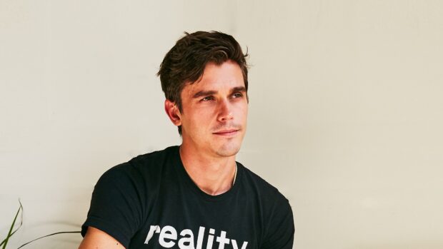Antoni Porowski wearing a black shirt with text sitting against a light wall, HD Desktop Wallpaper