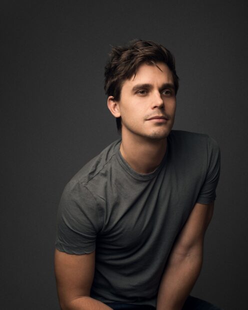 Antoni Porowski sits with a thoughtful expression wearing a grey t shirt against a dark background, HD Mobile Wallpaper