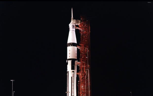 The Apollo 13 rocket stands ready at the launch pad with the USA flag and launch tower, 2K Desktop Wallpaper