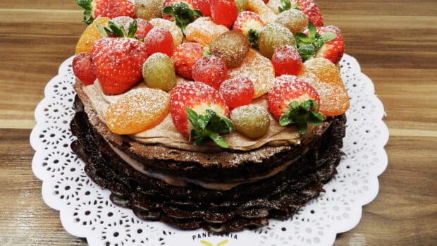A chocolate cake decorated with apricots, strawberries, grapes, and powdered sugar on a white doily, 4K Desktop Wallpaper