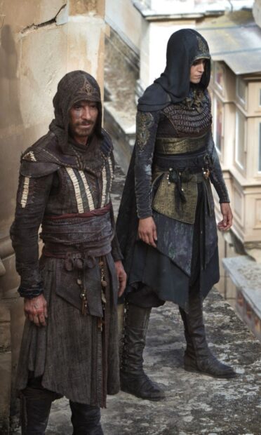 Two Assassins Creed movie characters stand on an ancient stone balcony with medieval attire, HD Mobile Wallpaper