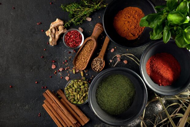 Various seasoning spices including cinnamon and herbs arranged on a black table, HD Desktop Wallpaper