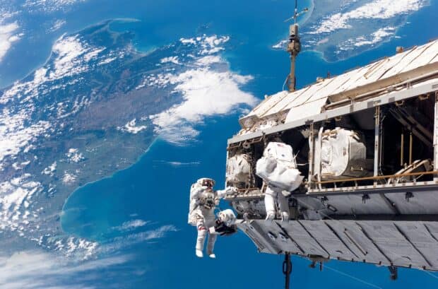 Two astronauts in spacesuits performing a spacewalk outside a space station against Earth view, 2K Desktop Wallpaper