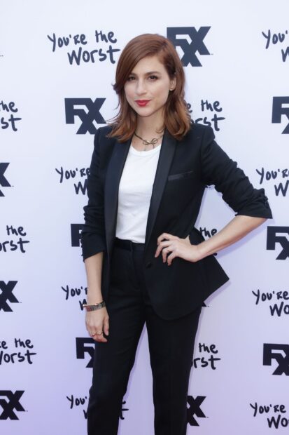 Aya Cash stands confidently in a black suit at the FX You're the Worst backdrop, HD Mobile Wallpaper
