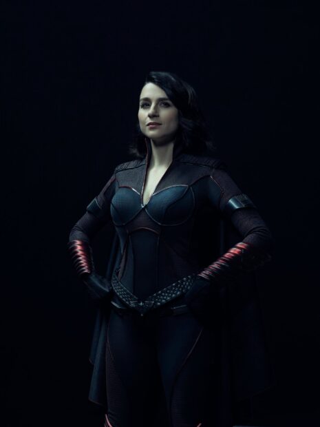 Aya Cash in a dark superhero costume standing confidently with hands on hips, 2K Phone Wallpaper