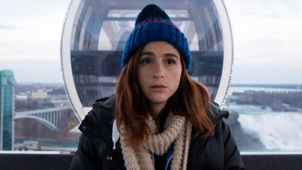 Aya Cash wearing a blue knit hat and scarf sitting inside a cabin with a city view, 4K Desktop Wallpaper