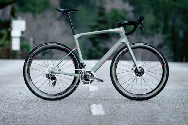 A sleek BMC bike is standing on a deserted road surrounded by blurred greenery, HD Desktop Wallpaper