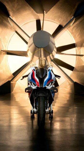 A BMW M 1000 RR motorcycle is displayed in front of a large fan with lights, 4K Mobile Wallpaper
