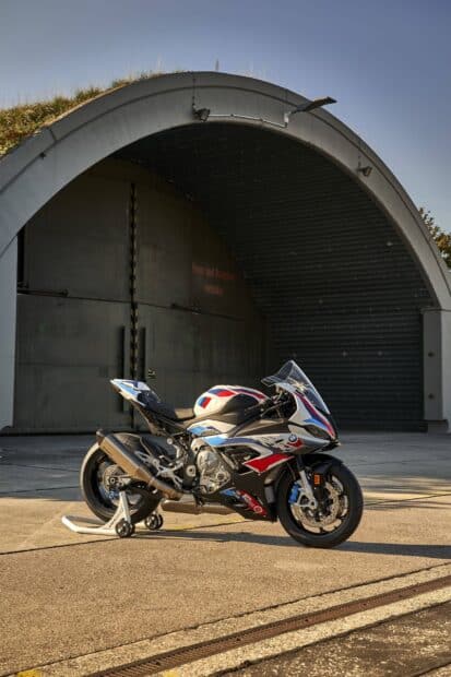 A BMW M 1000 RR motorcycle is parked outside a large hangar door, HD Desktop Wallpaper