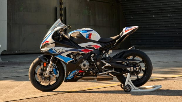 A BMW M 1000 RR motorcycle is parked outdoors on a stand near a concrete wall, 4K Desktop Wallpaper