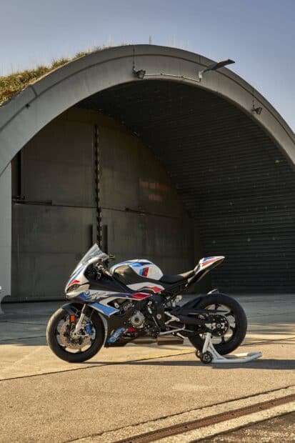 A BMW M 1000 RR motorcycle parked in front of a large hangar with clear skies, HD Desktop Wallpaper