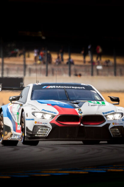 A BMW race car is competing intensely on the race track with blurred spectators in the background, 2K Mobile Wallpaper