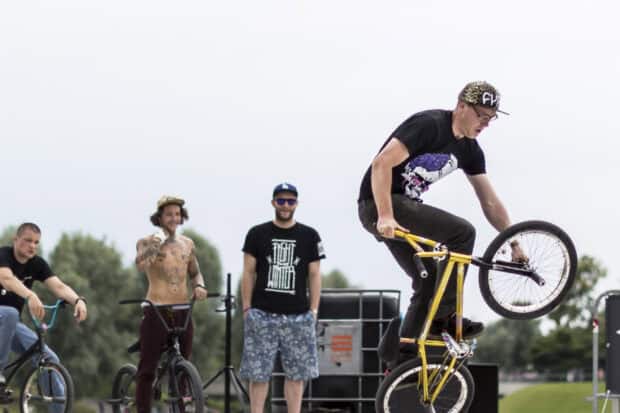 A BMX rider performs a front wheel trick while others watch in the park, 2K Desktop Wallpaper