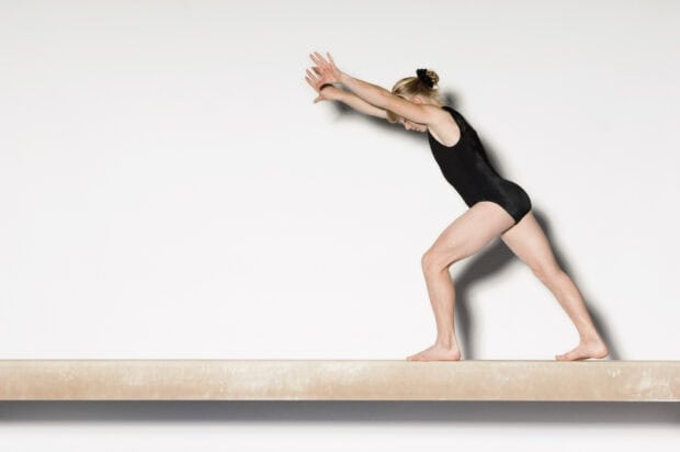 A gymnast is performing a balance beam move in a black leotard, HD Desktop Wallpaper