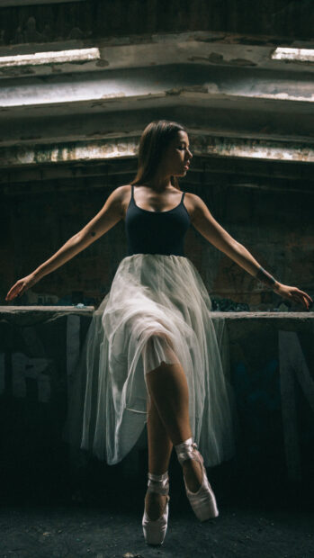 A ballet dancer stands on pointe in a dimly lit urban setting, 4K Mobile Wallpaper