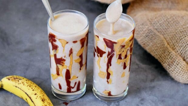 Two glasses of banana milkshake with chocolate drizzles and a ripe banana on the side, HD Desktop Wallpaper