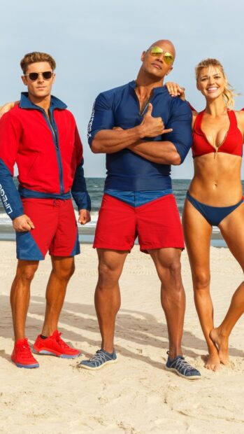 The Baywatch movie cast is standing together by the ocean in vibrant beachwear, HD Mobile Wallpaper