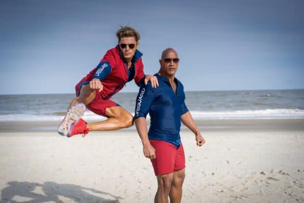 Two lifeguards pose on the beach with one jumping near the ocean, HD Desktop Wallpaper