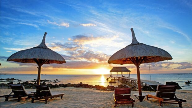 Two large beach umbrellas shading wooden lounge chairs on the sandy coast at sunset, 4K Desktop Wallpaper