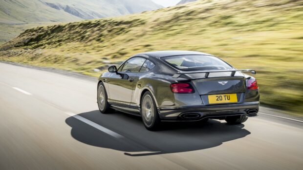 A black Bentley Continental GT is driving fast on a winding mountain road with green hills in the background, 4K Desktop Wallpaper