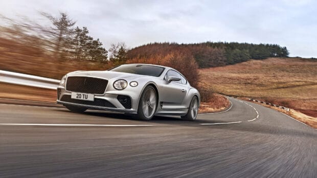 A silver Bentley Continental GT is speeding along a curvy road surrounded by autumn trees, 2K Desktop Wallpaper