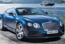 A blue Bentley Continental GT parked near a calm lake with a ferry in the background, 4K Desktop Wallpaper