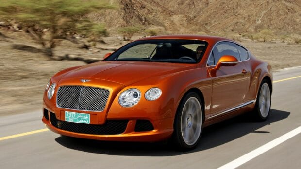 A sleek Bentley Continental GT is driving on a desert road with rocky hills in the background, 4K Desktop Wallpaper