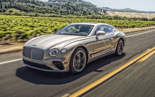 A silver Bentley Continental GT drives along a highway near green vineyards, 2K Desktop Wallpaper