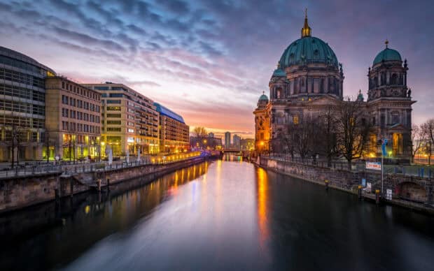 Berlin Cathedral stands beside the river during sunset with glowing city lights and a colorful sky, 2K Desktop Wallpaper