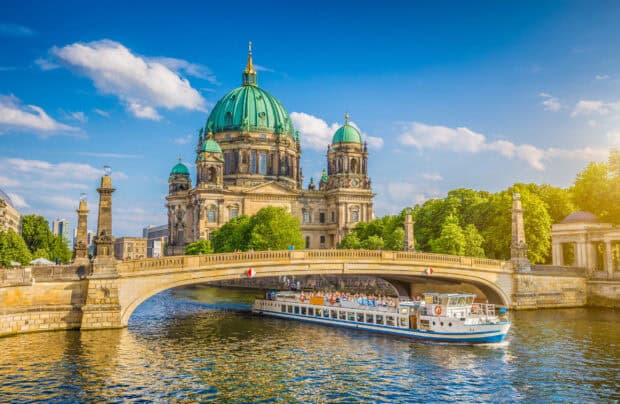 A tourist boat passes under a stone bridge near Berlin Cathedral with blue skies, 2K Desktop Wallpaper