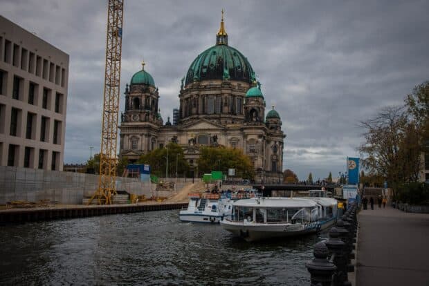 The Berlin Cathedral stands prominently by the river with boats passing in front under a cloudy sky, HD Desktop Wallpaper