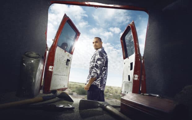A man stands in desert landscape with open van doors and tools inside against a blue sky, 2K Desktop Wallpaper