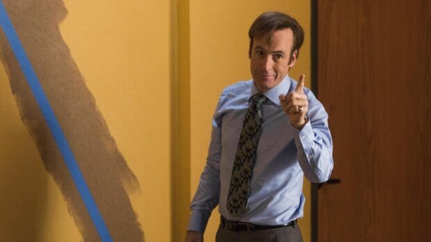 A man in a blue shirt points a finger with a confident smile in an office setting, 2K Desktop Wallpaper