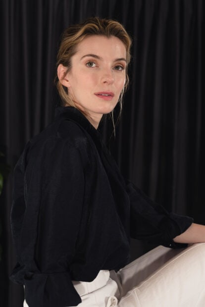 Betty Gilpin appears confident in a black shirt and light pants in this portrait, HD Mobile Wallpaper
