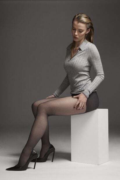 Betty Gilpin sits on a white block wearing a gray top and black heels, HD Mobile Wallpaper