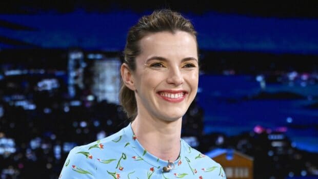 Betty Gilpin is smiling warmly while wearing a blue floral dress during a talk show, HD Desktop Wallpaper