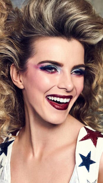 Betty Gilpin is smiling brightly with colorful glitter makeup and styled hair, 4K Mobile Wallpaper