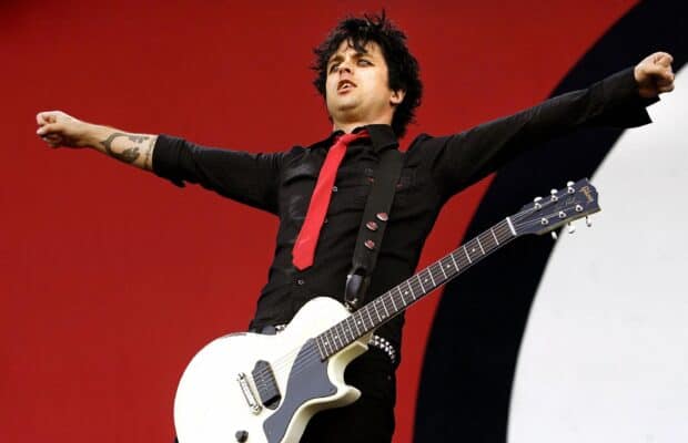 Billie Joe Armstrong is playing guitar with arms spread wide on a bold red background, 2K Desktop Wallpaper