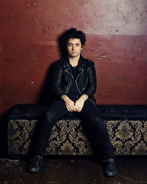 Billie Joe Armstrong sitting on patterned bench with a red wall background, HD Desktop Wallpaper
